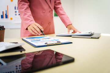 A businesswoman in a pink suit works at a desk with a whiteboard in the background. She focuses on accounting and financial services, professionalism and expertise in various financial roles.