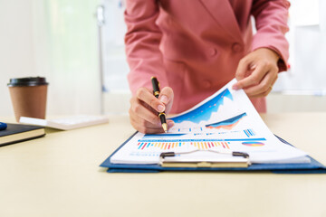 A businesswoman in a pink suit works at a desk with a whiteboard in the background. She focuses on accounting and financial services, professionalism and expertise in various financial roles.