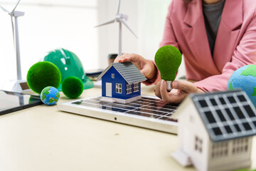 A businesswoman in a pink suit stands at a white desk with a world model, electric car model, and green light bulb, promoting Earth Day, green energy, and sustainability efforts.