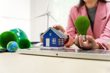 A businesswoman in a pink suit stands at a white desk with a world model, electric car model, and green light bulb, promoting Earth Day, green energy, and sustainability efforts.