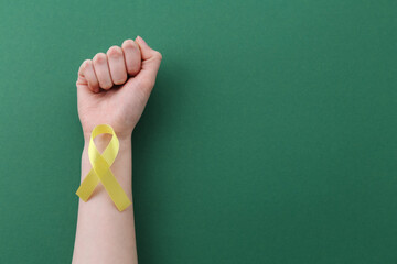 Woman with yellow awareness ribbon on green background, top view. Space for text