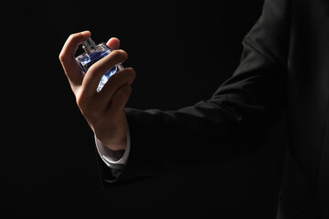 Fototapeta premium Man spraying luxury perfume on dark background, closeup