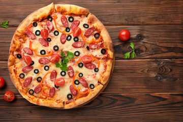 Tasty pizza with dry smoked sausages, tomatoes, olives, pepper and parsley on wooden table, top view. Space for text