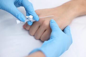 Nurse inputting catheter for IV drip in patient hand, closeup