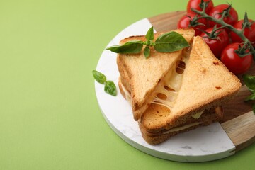 Pieces of toasted bread with melted cheese, tomatoes and basil on green background, space for text