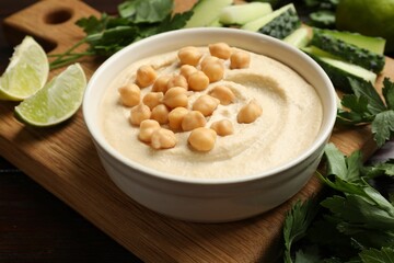 Tasty hummus with chickpeas in bowl and fresh products on table, closeup