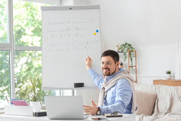 Young male teacher math with laptop and formulas on whiteboard giving online lesson at home