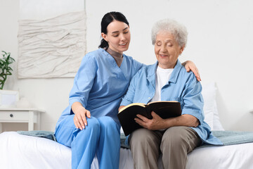 Fototapeta premium Caregiver reading Bible with senior woman at home