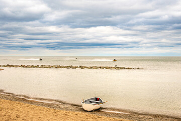 personal watercraft, traveling at speed from left to right, with a traditional white rowboat pulled up at the water's edge on kew beach in toronto's beaches neighbourhood room for text