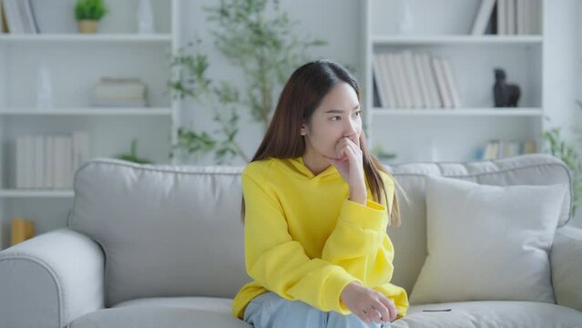 Young Asian woman with feeling sad and stressed, sick and headache, sitting on sofa in living room at home