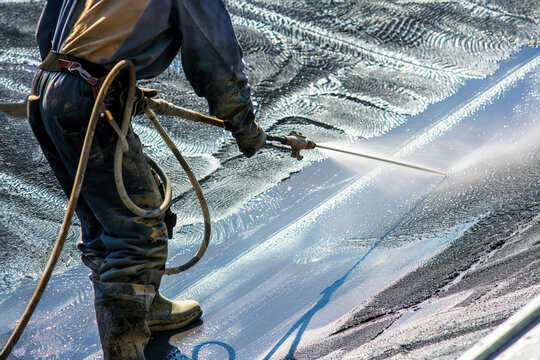 Construction site with worker using water shotcrete hose, concrete texture visible.