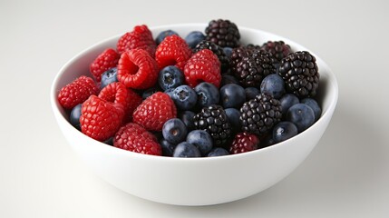 A white bowl filled with fresh raspberries, blackberries, and blueberries on a white background. Healthy and delicious mixed berries assortment.