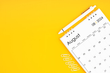 August 2024, Monthly desk calendar for 2024 year and pen with paper clips on yellow color...