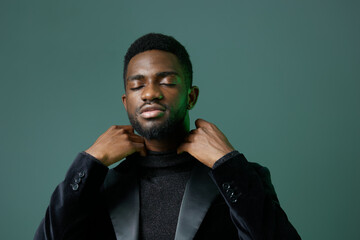 Young african american man in a black tuxedo, adjusting his bow tie with a confident expression