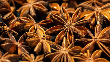 Brown Anise stars as pattern at sunlight, close up aromatic spices dried aniseed on black background, aesthetic food pattern, textural graphic banner, natural season condiments