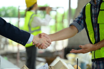 Cropped shot of businessman in black suit and engineer shaking hands with successful project on construction site