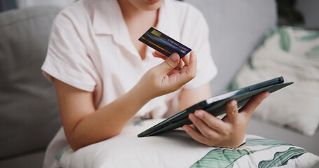 Fototapeta premium Selective focus, Hands of young woman using credit card to pay on digital tablet in the living room at home ,Buy things online by tablet, Pay online.