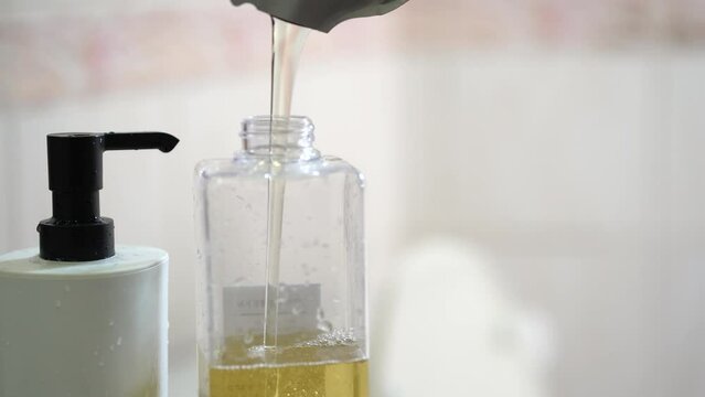 A man fills a dispenser with liquid soap by pouring it from a refill to reduce plastic waste. Soap or Shampoo for refill.