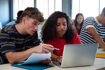 Caucasian teen boy and black teenage female high school students in class working together using...
