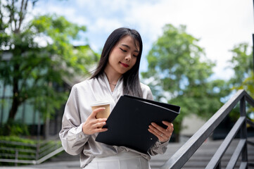 Fototapeta premium A businesswoman is looking at her document folder with a proud expression while standing outdoors.