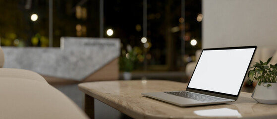A laptop computer on a neutral marble coffee table in a modern lobby lounge at night.
