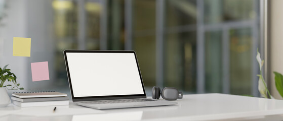 A modern office features a laptop computer with a white-screen mockup on a white desk.