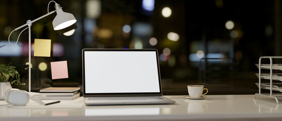 A laptop computer and accessories on a table against the window with a night city view.