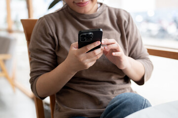 A cropped image of an Asian woman in casual clothes is using her smartphone while chilling in a cafe