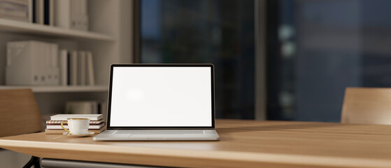 A laptop computer with a white-screen mockup on a wooden meeting table in a modern meeting room.