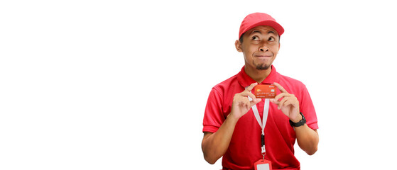 Pensive Asian delivery man or courier gazes thoughtfully at empty copy space while holding a credit card, isolated on a white background. Concept of financial planning, transactions, delivery services