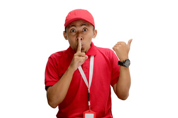 Asian delivery man is pointing to an empty space while placing his fingers on his lips, signaling...