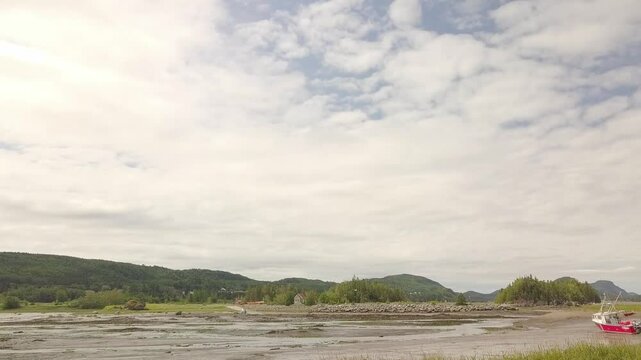Video with a drone showing a sky with white clouds and blue background, the Bic mountains and a small boat at low tide.
