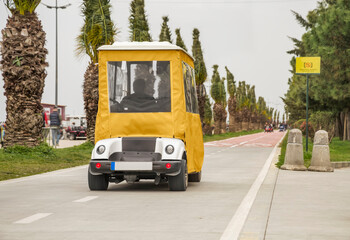 An electric scooter-car with a yellow polyethylene top is riding along the bike path