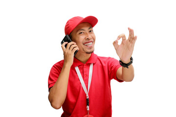 Excited Asian delivery man or courier having an engaging phone call with a customer, showing an OK gesture to indicate agreement or approval. Isolated on a white background.