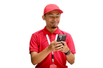 A cheerful Asian delivery man or courier, wearing a red cap and red polo shirt, texting on his phone, receiving good news about a successful transaction or delivery. Isolated on a white background