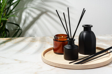 Black Reed Diffuser, Amber Candle, and Wooden Tray on White Surface