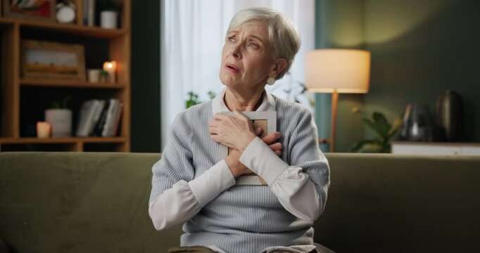Senior, woman and sad with photo in home for grief, memory and mourning on sofa with hugging lost love. Elderly, person and depression for picture frame with remember, thinking and nostalgia on couch