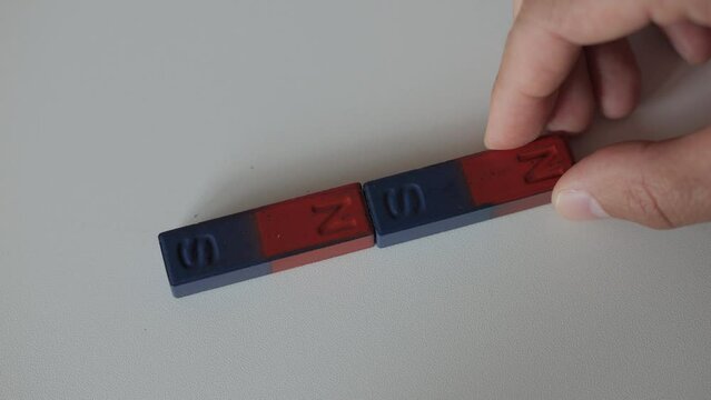 Science Educational Experiment With Magnets. Man Hand Moves Two Magnets Around So That They Attract And Repel Each Other. Magnetic Force Demonstration Showing Attraction And Repulsion.