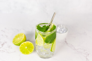 Mojito cocktail with lime, mint and ice on the white marble, light background. Sparkling refreshing water. Space for text. 