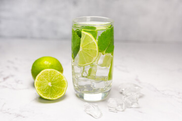 Mojito cocktail with lime, mint and ice on the white marble, light background. Sparkling refreshing water. Space for text. 