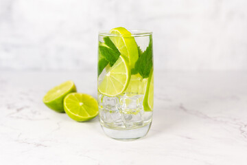 Mojito cocktail with lime, mint and ice on the white marble, light background. Sparkling refreshing water. Space for text. 