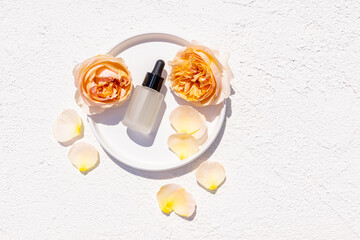 Natural cosmetic product in glass bottles with dropper on white tray and embossed background with yellow tea rose head flower. Care, beauty.