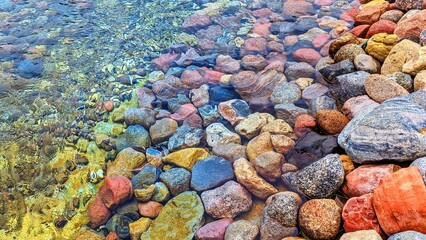 Colored stones on the shore and in the water. Transparent, clean water. Ecology. Panoramic photo.