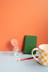 Workspace object. Notebook, colored pencil, vase of plant, mug cup on gray desk. red wall background