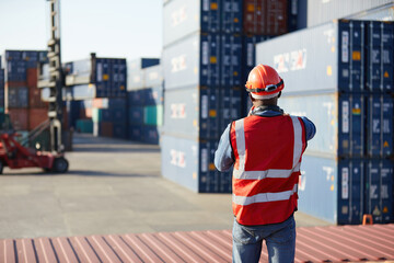 back view African factory worker or engineer using walkie talkie and showing stop gesture to crane car in containers warehouse storage