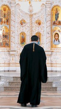 Interior of the church with icons,The Christian church with the iconostasis. Media. Rear view of a priest in front of iconostasis. Vertical video.