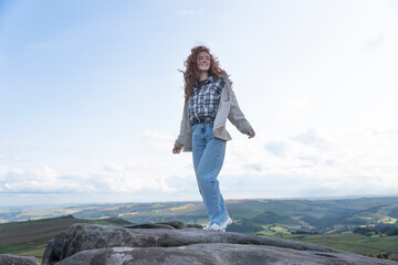 Naklejka premium Young Woman Hiking on Mountaintop With Rolling Hills in Distance