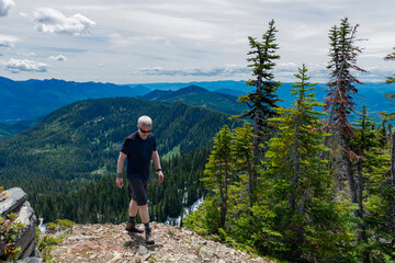 Adventurous athletic male hiker walking on a mountain top on a sunny day with rugged mountains in the background in the Pacific Northwest.