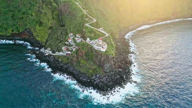 Wide aerial pan of Farol do Arnel lighthouse on seaside hill at Azores