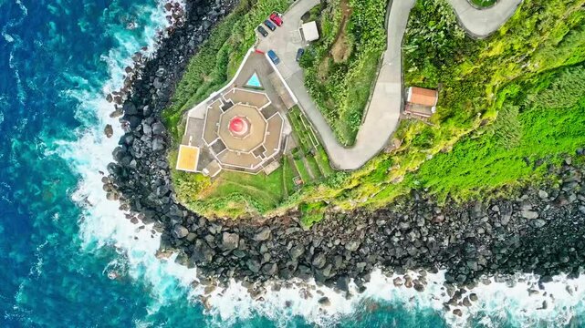 Aerial topdown view of beautiful Arnel lighthouse on rugged headland by Atlantic Ocean waves, Azores